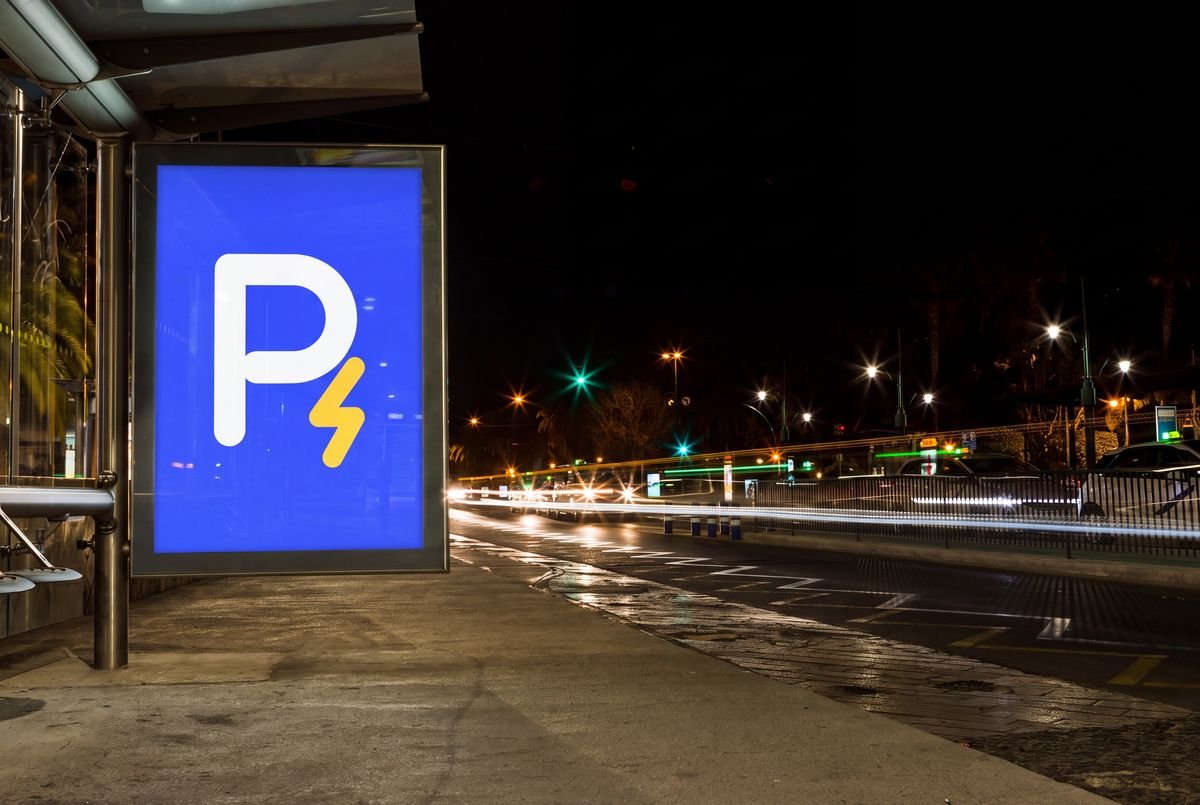 Aviso luminoso azul con el símbolo de Recargados, una P blanca con un rayo dorado, en un paradero junto a una avenida de noche.