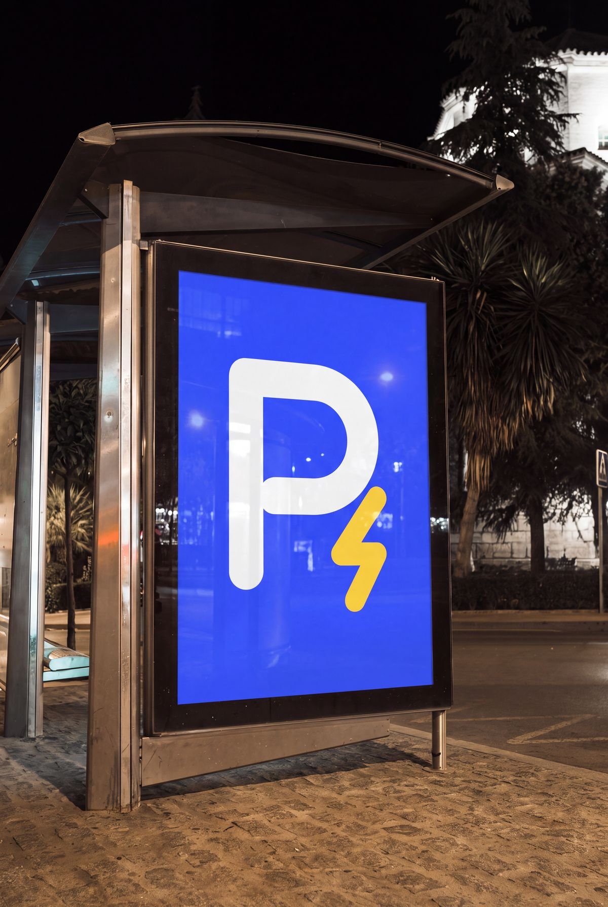 Aviso azul con el símbolo de Recargados, una P blanca con un rayo dorado, en un paradero de bus de noche.