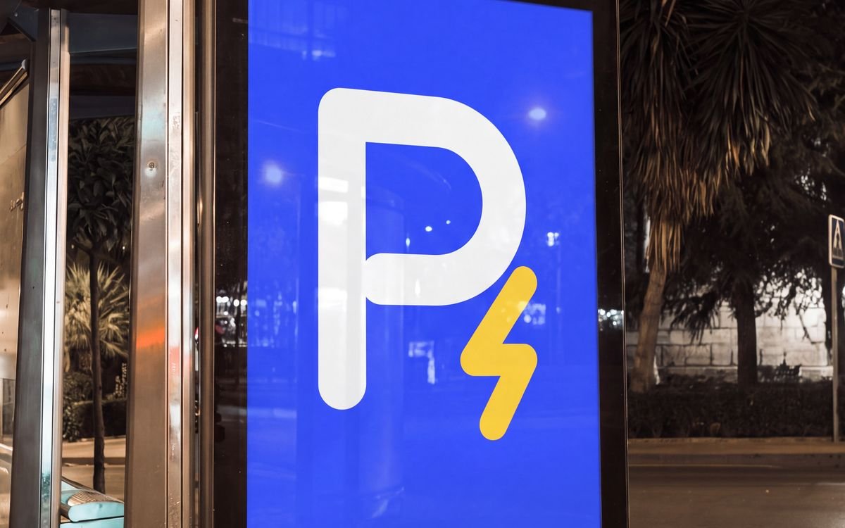 Aviso azul con el símbolo de Recargados, una P blanca con un rayo dorado, en un paradero de bus de noche.