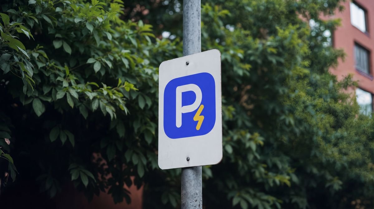 Señal de parqueadero con el símbolo de Recargados, una P blanca con un rayo dorado, en una calle con árboles.